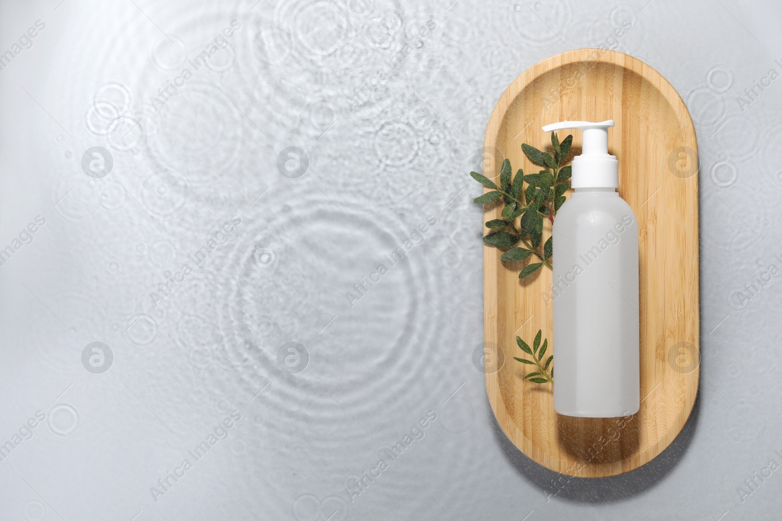 Photo of Wooden tray with bottle of facial cleanser and leaves in water on light grey background, top view. Space for text