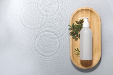 Photo of Wooden tray with bottle of facial cleanser and leaves in water on light grey background, top view. Space for text