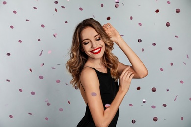 Photo of Happy young woman and confetti on grey background. Christmas celebration