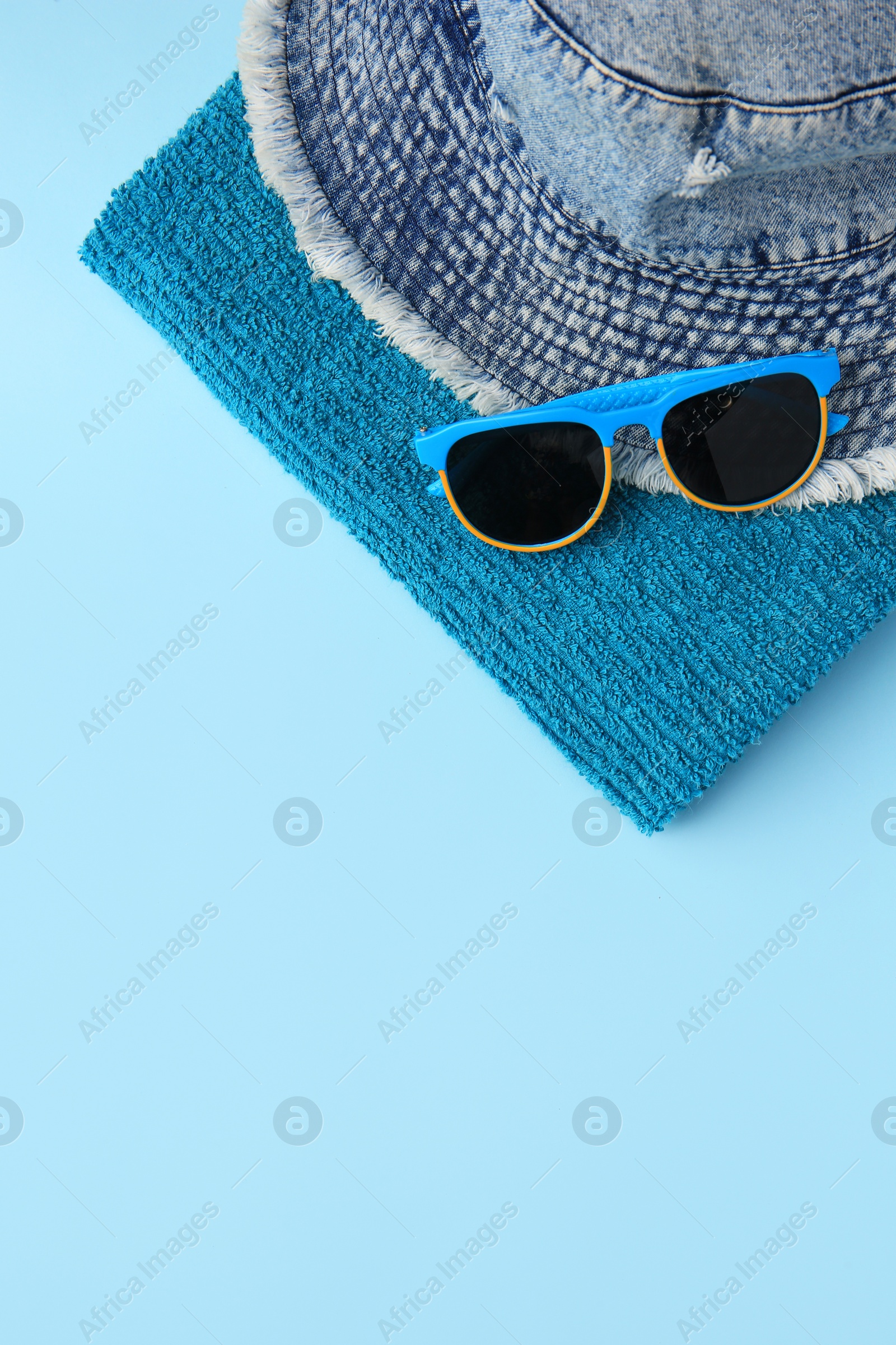 Photo of Towel, denim hat and sunglasses on light blue background, flat lay with space for text. Beach accessories