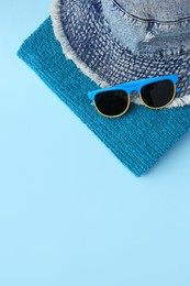 Photo of Towel, denim hat and sunglasses on light blue background, flat lay with space for text. Beach accessories