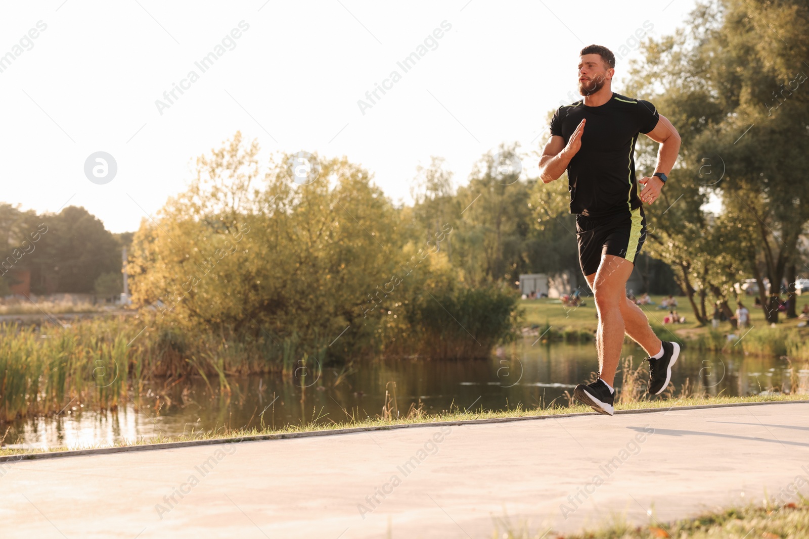 Photo of Young man running near pond in park. Space for text