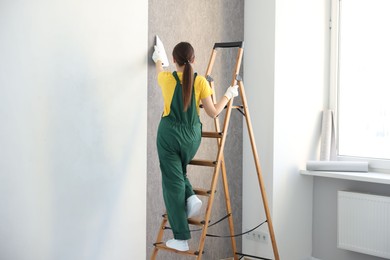 Photo of Woman smoothing stylish gray wallpaper in room, back view