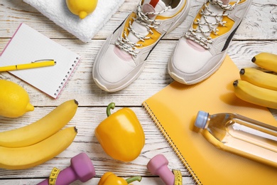 Photo of Flat lay composition with sport items, healthy food and notebooks on wooden background. Weight loss concept