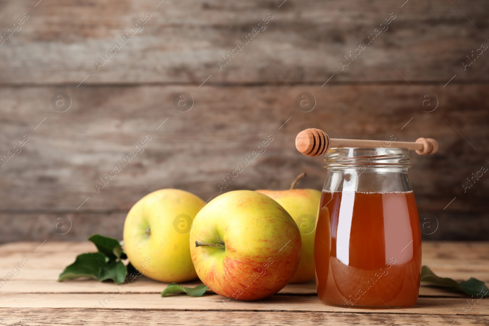 Photo of Jar of honey, dipper and apples on wooden table