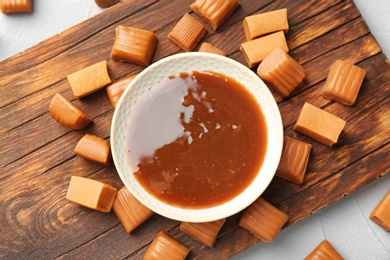 Delicious candies and caramel sauce on wooden board, top view