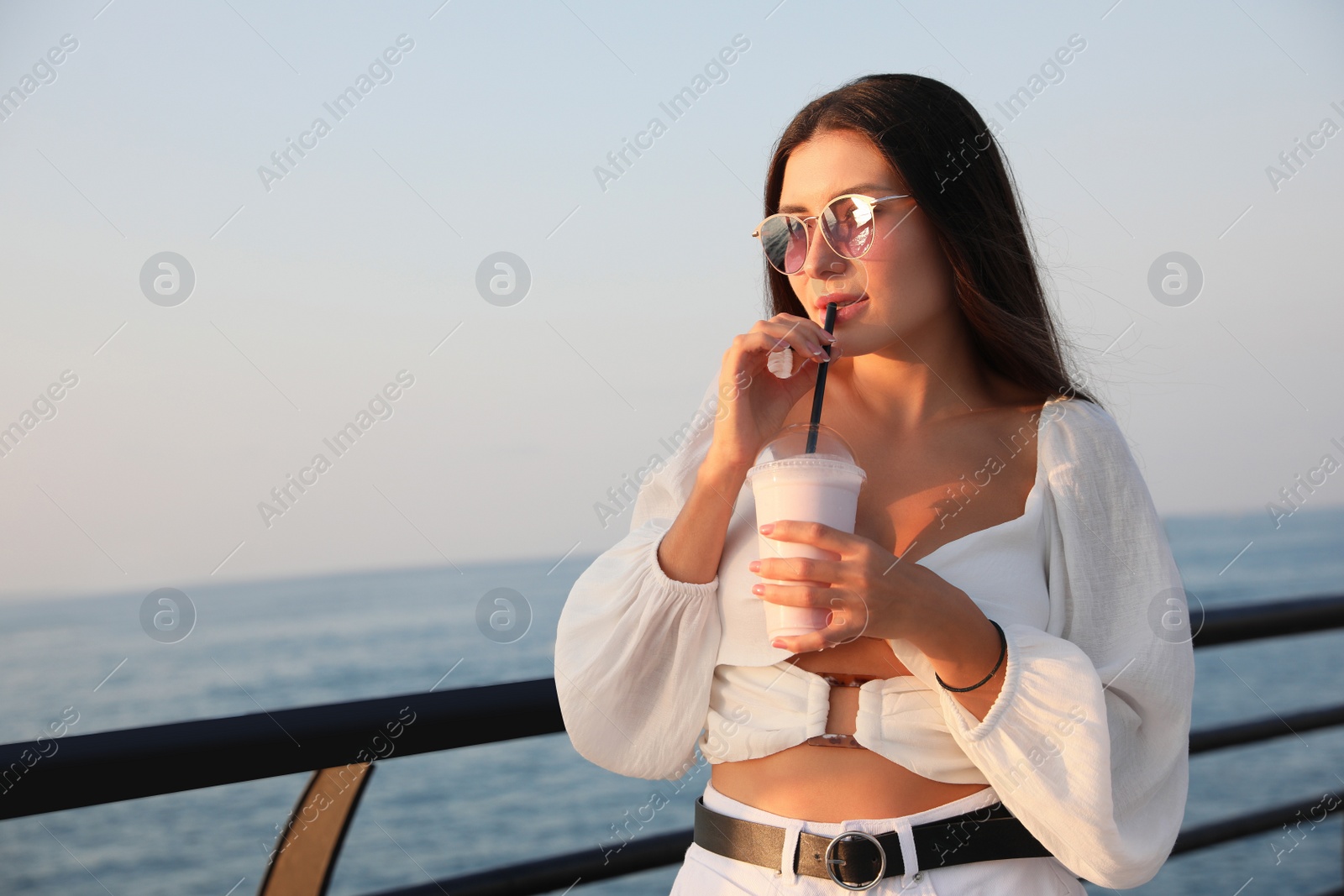 Photo of Beautiful woman with tasty milk shake near sea, space for text