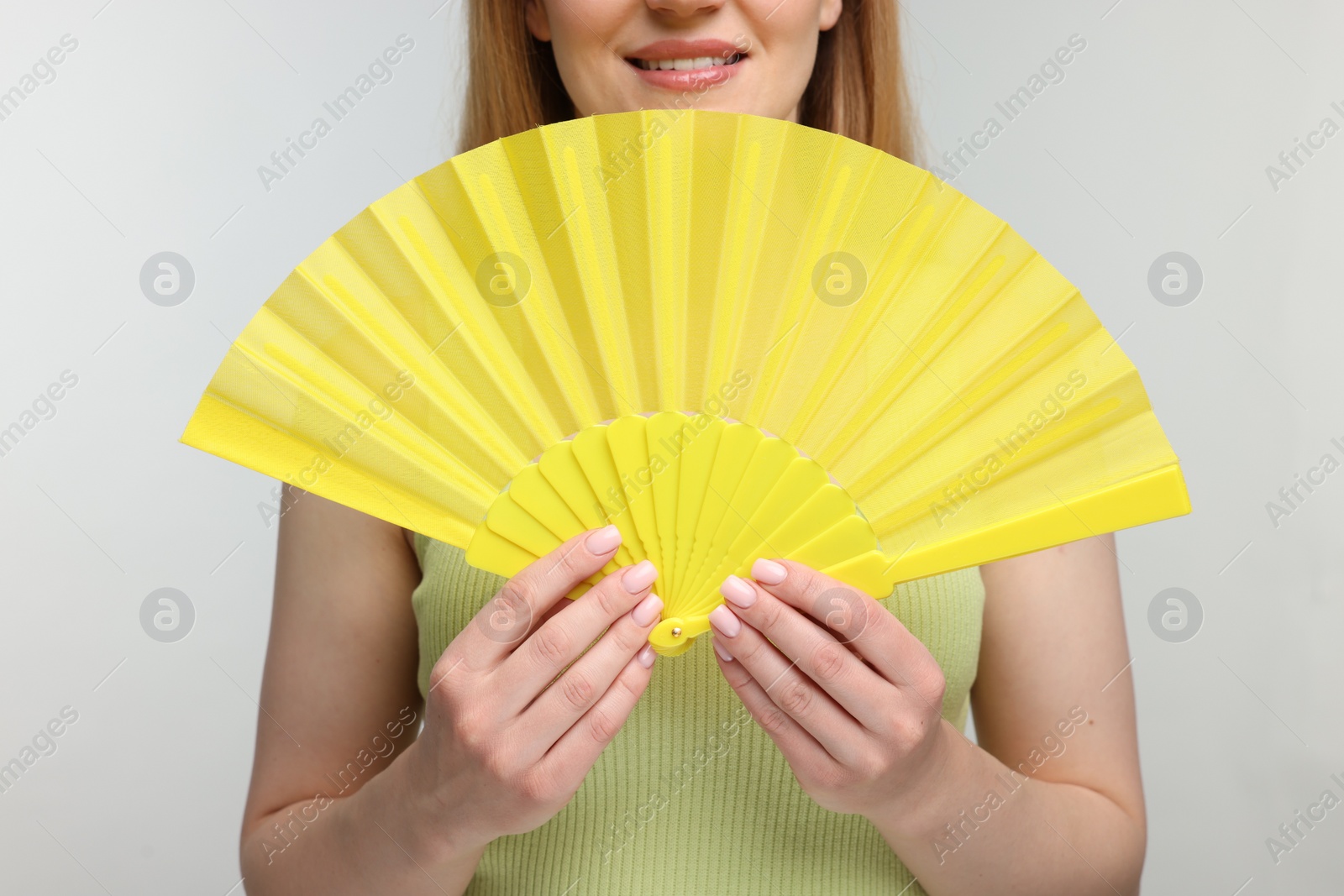 Photo of Woman with yellow hand fan on light grey background, closeup