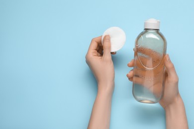 Woman holding makeup remover and cotton pad on light blue background, top view. Space for text