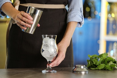 Photo of Woman preparing fresh alcoholic cocktail with ice at bar counter, closeup
