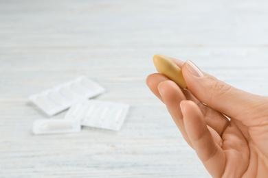 Photo of Woman holding suppository at white wooden table, closeup. Hemorrhoid treatment