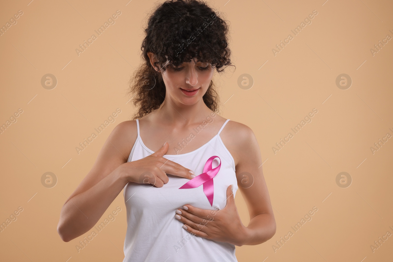 Photo of Breast cancer awareness. Beautiful young woman with pink ribbon doing self-examination on light brown background