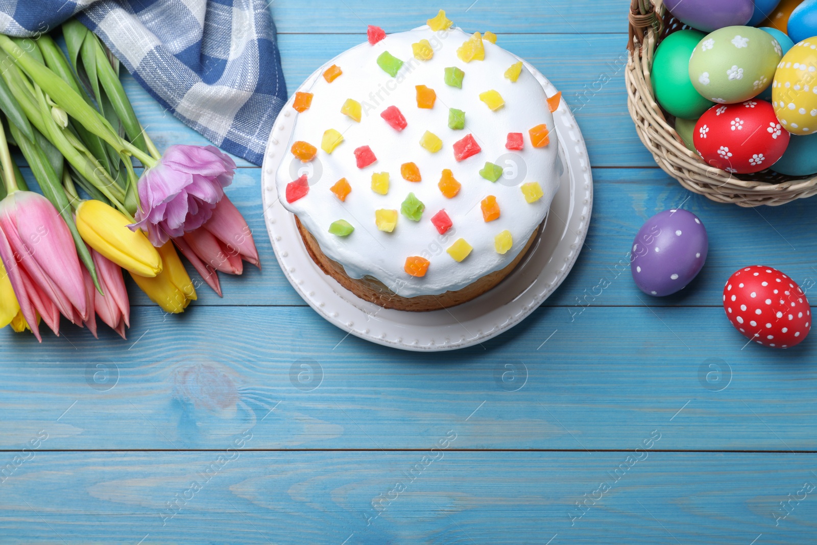 Photo of Easter cake, colorful eggs and tulips on blue wooden table, flat lay. Space for text