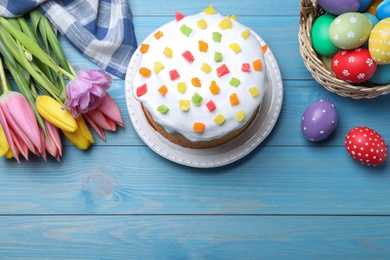 Photo of Easter cake, colorful eggs and tulips on blue wooden table, flat lay. Space for text