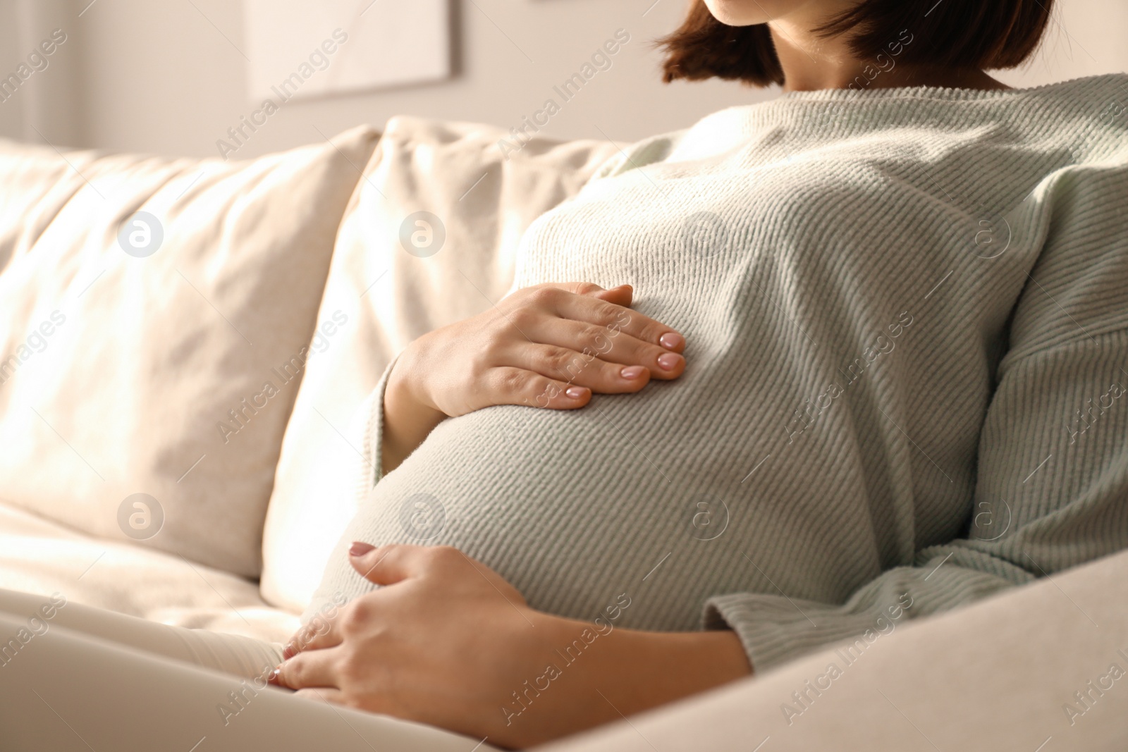 Photo of Pregnant young woman touching belly at home, closeup