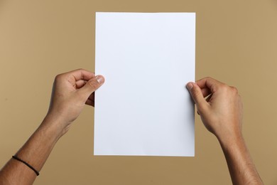 Photo of Man holding sheet of paper on beige background, closeup. Mockup for design