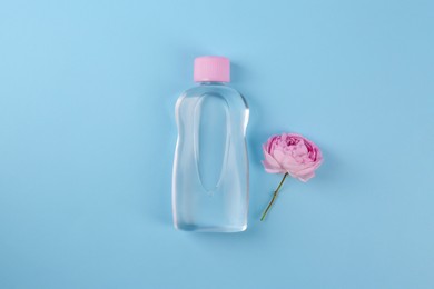 Photo of Bottle with baby oil and beautiful flower on light blue background, flat lay. Space for text