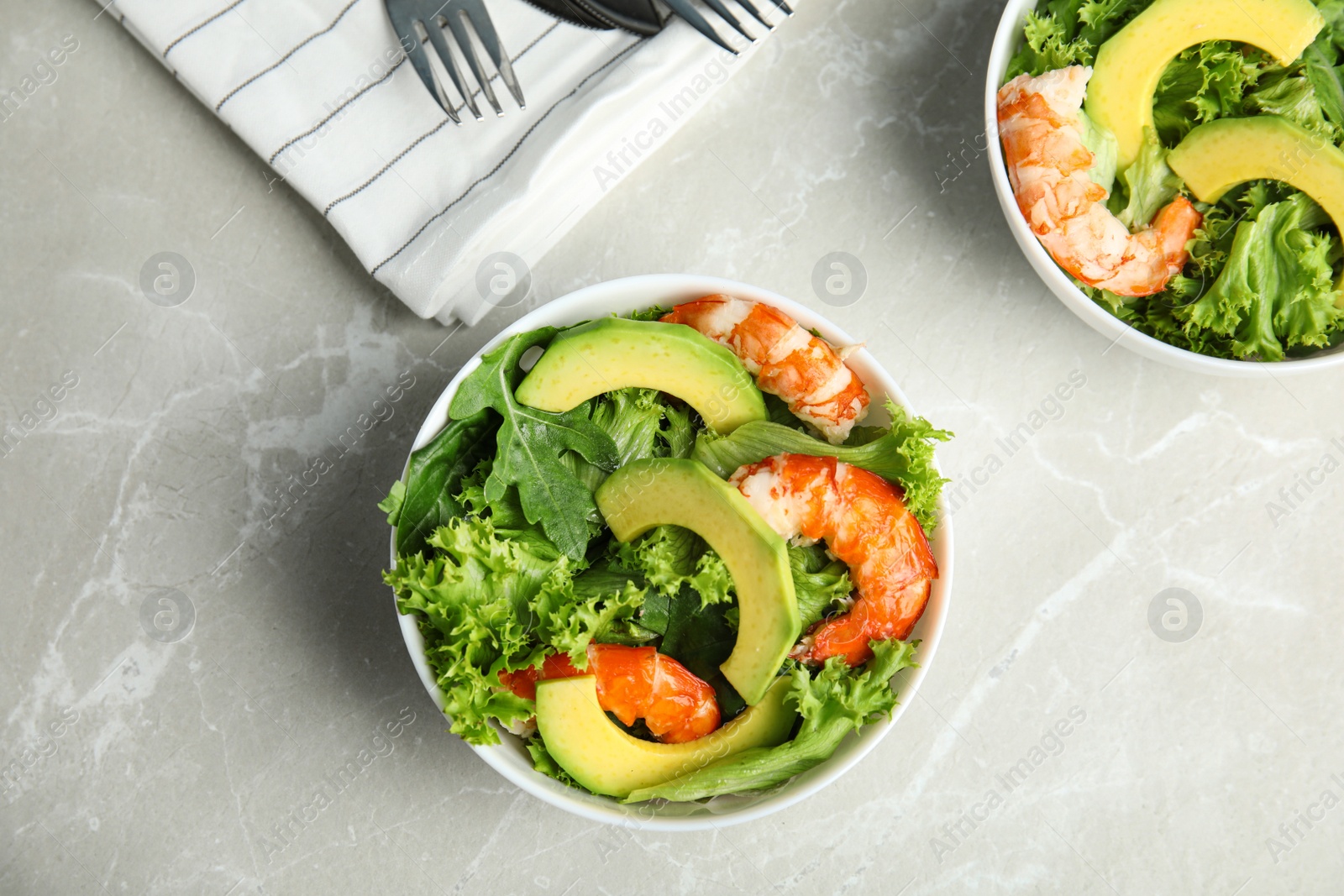 Photo of Delicious avocado salad with shrimps in bowls on grey marble table, flat lay