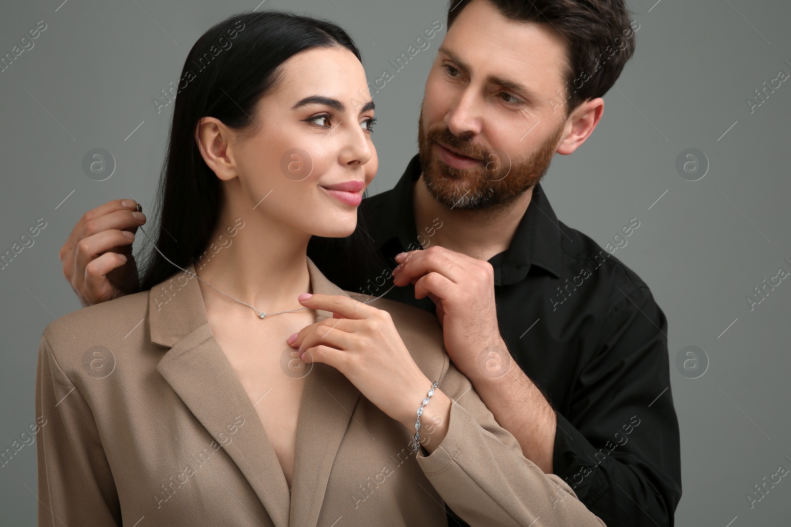 Photo of Man putting elegant necklace on beautiful woman against dark grey background