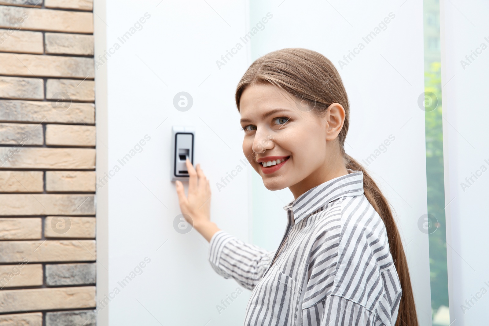 Photo of Young woman pressing fingerprint scanner on alarm system indoors