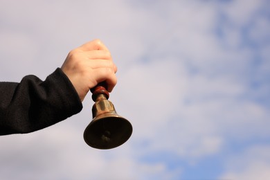 Pupil with school bell against cloudy sky, closeup. Space for text