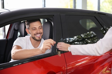 Female salesperson giving car key to man in auto dealership