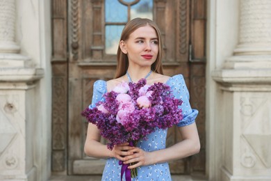 Photo of Beautiful woman with bouquet of spring flowers near building outdoors