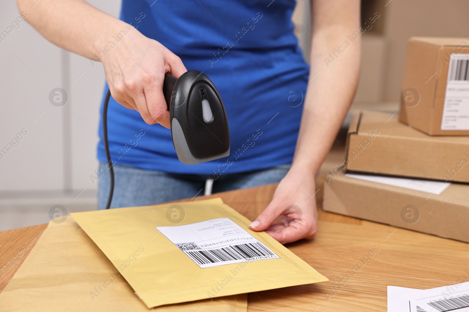 Photo of Parcel packing. Post office worker with scanner reading barcode at wooden table indoors, closeup