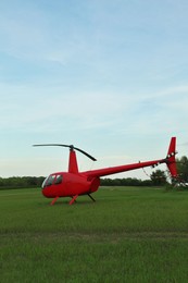 Photo of Modern red helicopter on green grass outdoors