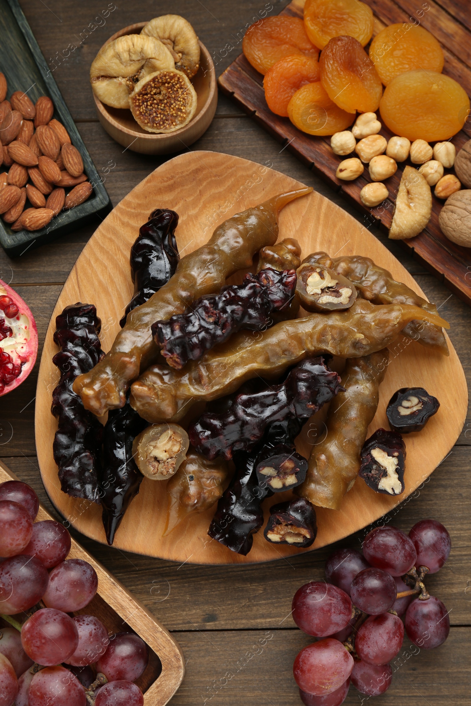 Photo of Delicious sweet churchkhelas and ingredients on wooden table, flat lay