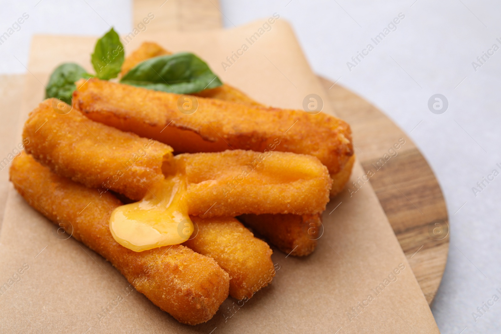 Photo of Tasty fried mozzarella sticks and basil on light table, closeup
