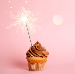 Birthday cupcake with sparkler on pink background