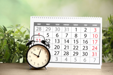 Calendar and alarm clock on wooden table against blurred green background