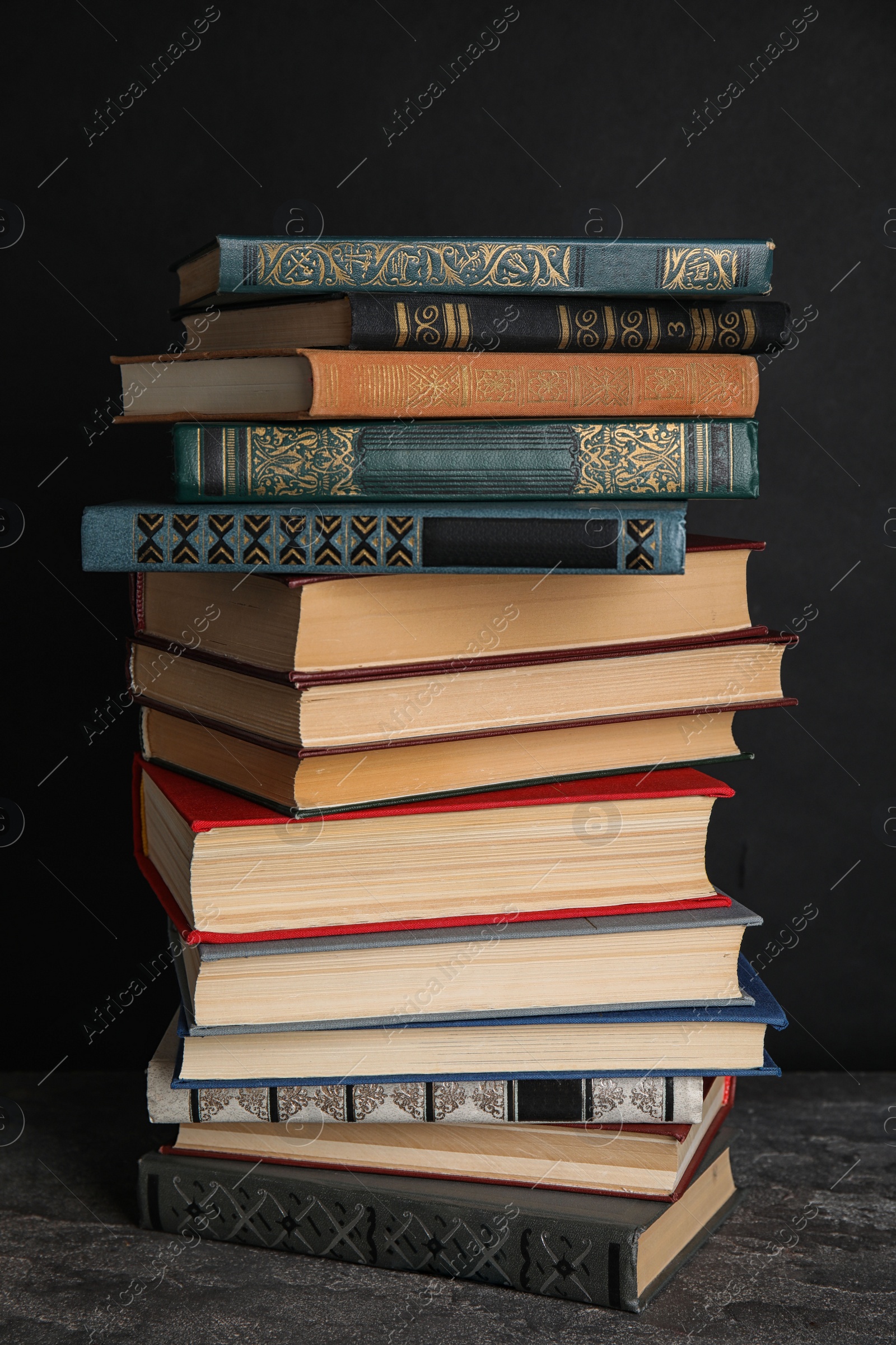 Photo of Stack of hardcover books on grey stone table against black background