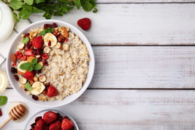 Photo of Delicious oatmeal with freeze dried berries, banana, nuts and mint served on white wooden table, flat lay. Space for text