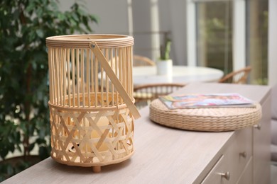 Photo of Stylish wicker holder with candle on chest of drawers indoors, space for text