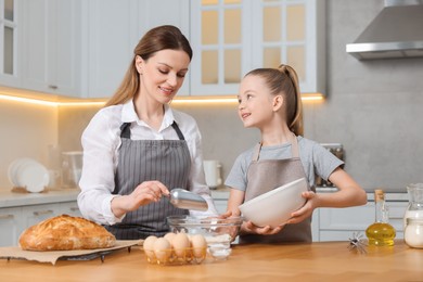 Photo of Making bread. Mother and her daughter preparing dough at wooden table in kitchen