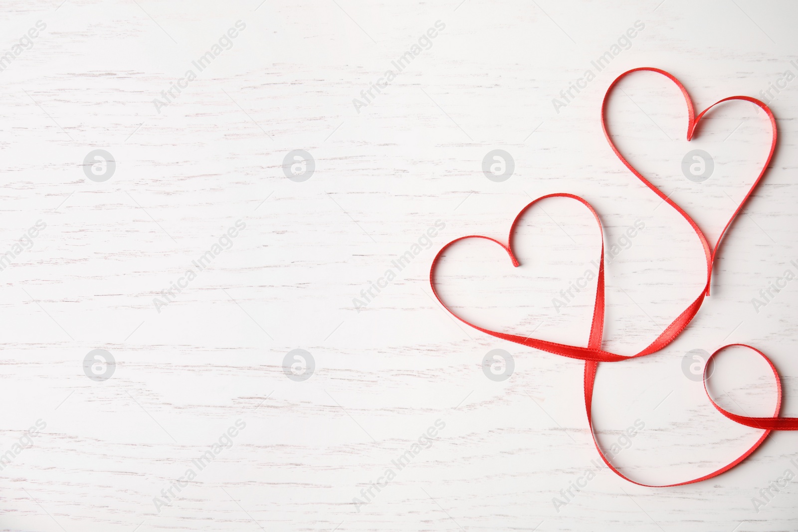 Photo of Hearts made of red ribbon on white wooden background, top view with space for text. Valentine's day celebration