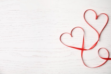 Photo of Hearts made of red ribbon on white wooden background, top view with space for text. Valentine's day celebration