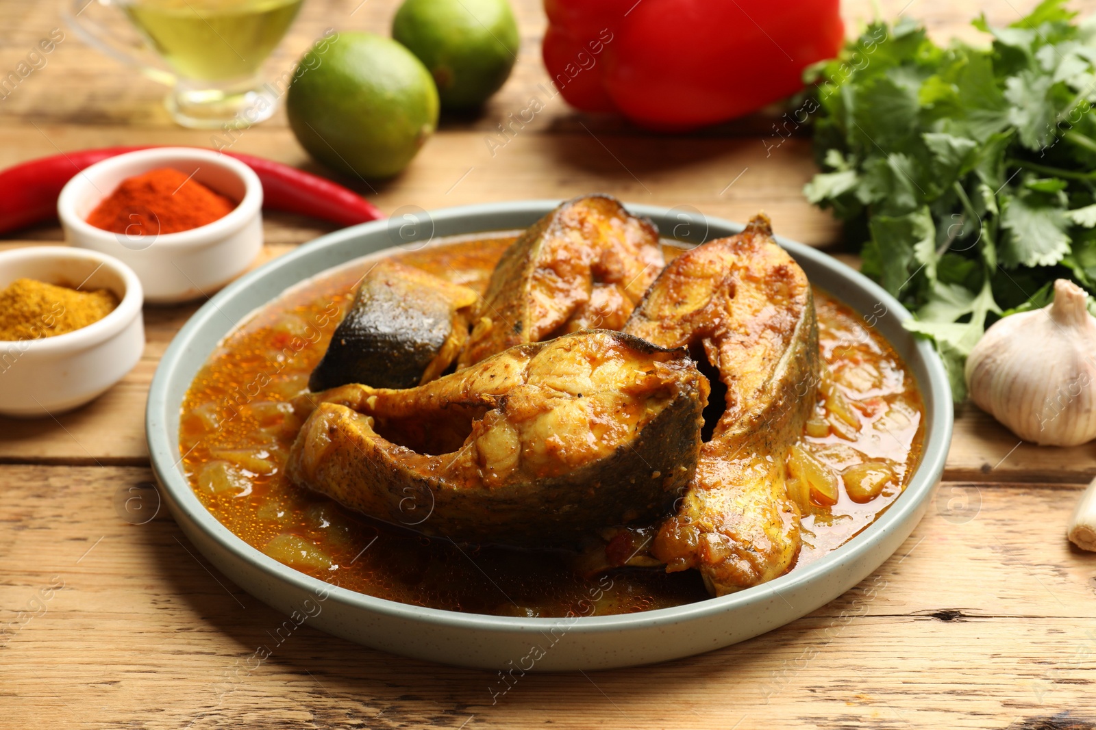 Photo of Tasty fish curry and ingredients on wooden table, closeup. Indian cuisine