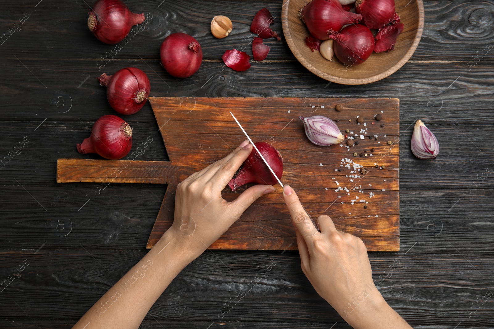 Photo of Woman cutting ripe red onion on wooden table, top view