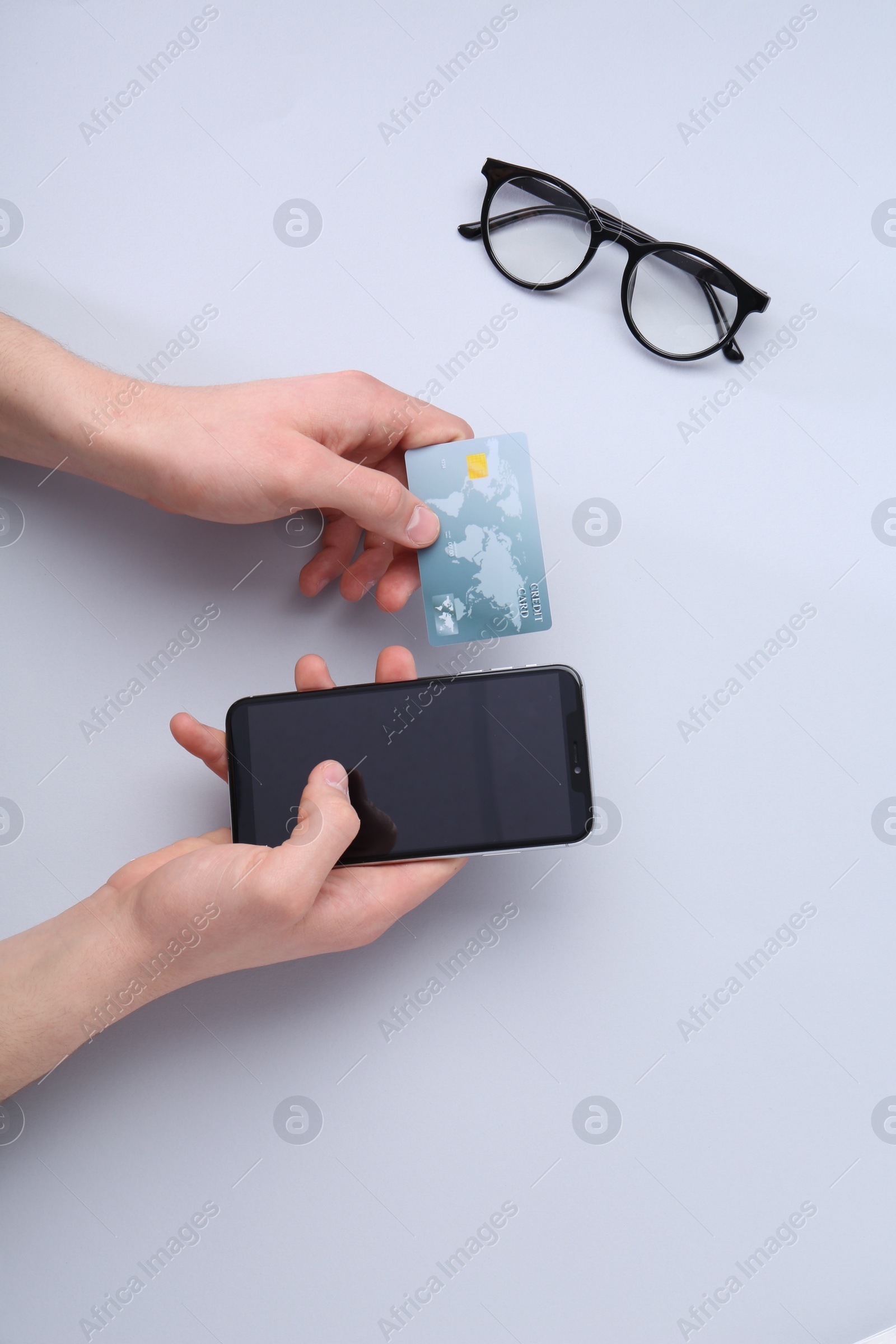 Photo of Online payment. Man with smartphone, credit card and glasses on light grey background, top view