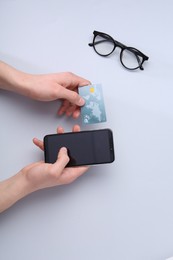 Online payment. Man with smartphone, credit card and glasses on light grey background, top view