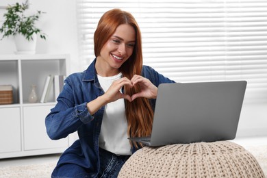 Woman making heart with hands during video chat via laptop at home. Long-distance relationship