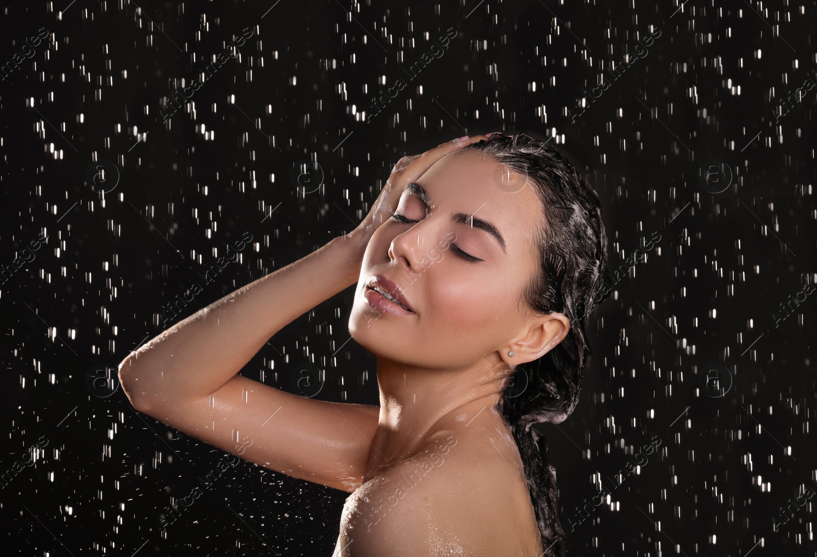 Photo of Young woman washing hair while taking shower on black background