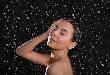 Photo of Young woman washing hair while taking shower on black background