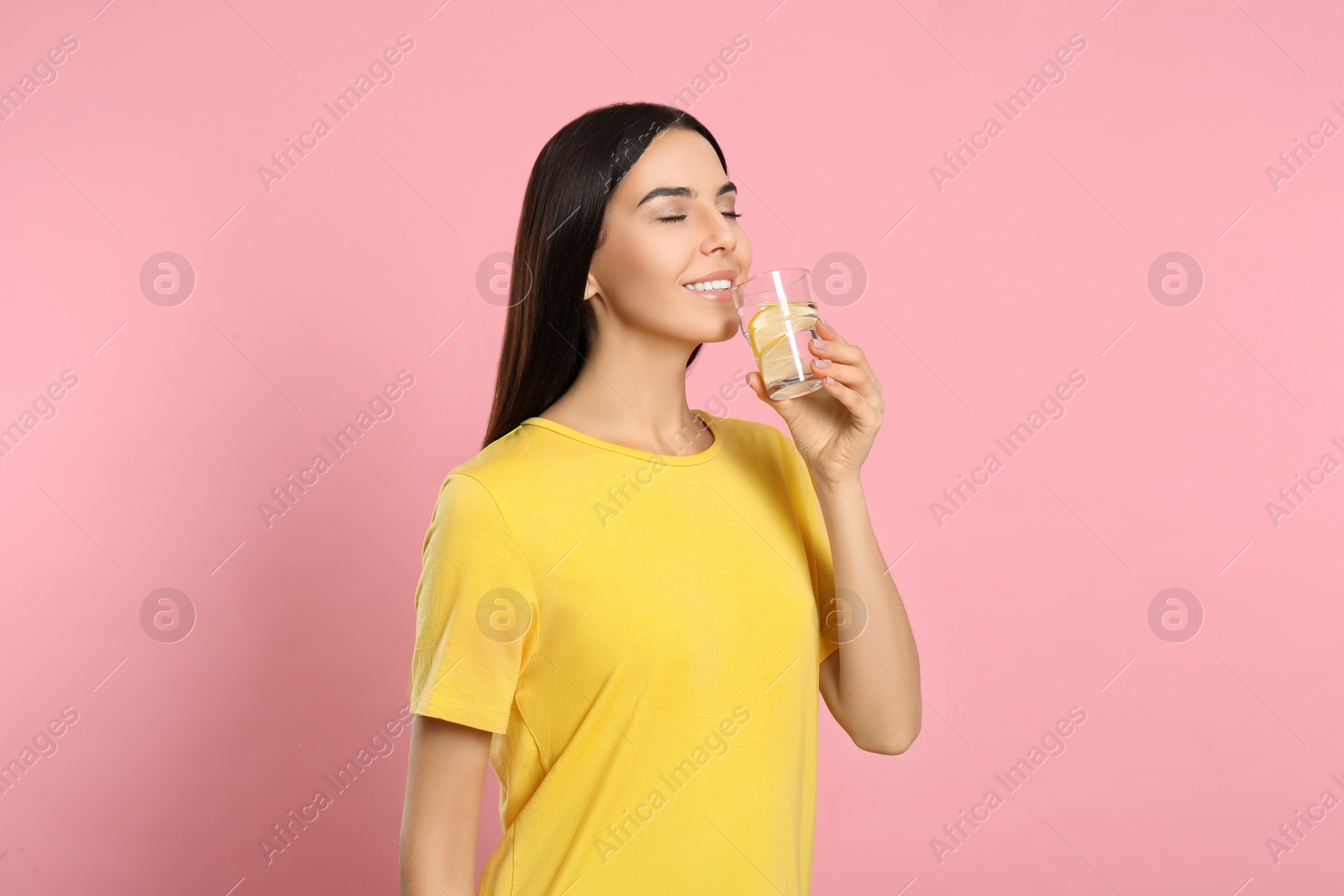 Photo of Beautiful young woman drinking tasty lemon water on pink background