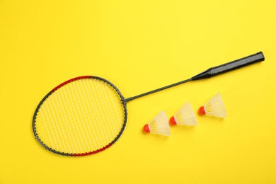 Photo of Racket and shuttlecocks on yellow background, flat lay. Badminton equipment