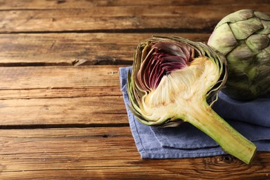 Photo of Cut and whole fresh raw artichokes on wooden table. Space for text