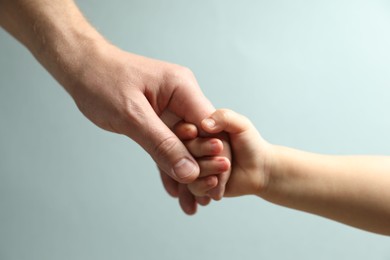 Photo of Father and child holding hands on light blue background, closeup